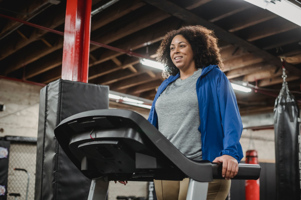 A smiling woman holds the side of a treadmill while walking