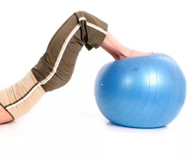 A woman lifts her lower body off the ground while resting her feet on an exercise ball